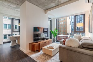 Ein modernes Wohnzimmer mit Flachbildfernseher, Holzmöbeln, einer Couch und großen Fenstern mit Blick auf die Stadt.