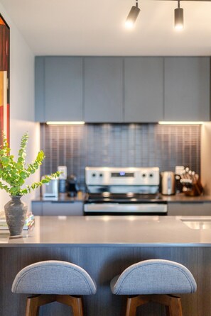 A modern kitchen with a central island, bar stools, and a potted plant. - Downtown Serenity Stay | Free Parking & Pool (Montréal)