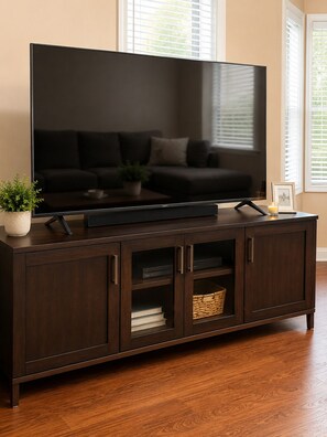 Ein dunkler Holz-Fernsehschrank mit Fernseher, einer Topfpflanze und einem gerahmten Bild.