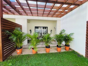Ein überdachter Patio-Bereich mit einem Holzzelt, Blumentöpfen und Blick auf ein Gebäude im Hintergrund.