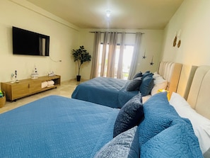 Ein Schlafzimmer mit zwei Betten, einem Fernseher, einer Pflanze und einem Fenster mit Vorhängen.