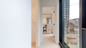 Interior moderno com um corredor que leva a um banheiro, uma janela grande com vista para a cidade e design minimalista.
