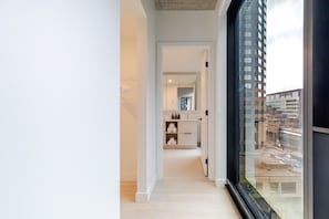 Ein modernes Interieur mit einem zur einem Badezimmer führenden Flur, einem großen Fenster mit Stadtblick und einem minimalistischen Design.