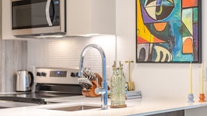 Cozinha moderna com micro-ondas, eletrodomésticos de aço inoxidável, um espaço bar com banquetas e um quadro abstrato colorido.