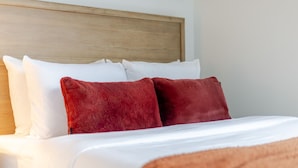Uma cama com almofadas brancas e vermelhas, cabeceira de madeira e manta marrom.