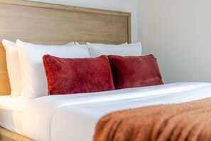 Ein Bett mit weißen und roten Kissen, einem Holz-Kopfteil und einer braunen Decke.