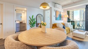 Een moderne woonkamer met een ronde houten tafel, een bank, een balkon met uitzicht en een grote spiegel.
