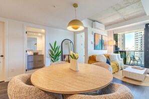 Ein modernes Wohnzimmer mit einem runden Holztisch, einer Couch, einem Balkon mit Aussicht und einem großen Spiegel.