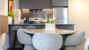 Een moderne keuken met grijze kastjes, een roestvrijstalen koelkast en een eethoek met een ronde tafel en grijze stoelen.