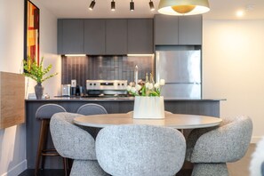 Eine moderne Küche mit grauen Schränken, einem Edelstahl-Kühlschrank und einem Essbereich mit rundem Tisch und grauen Stühlen.