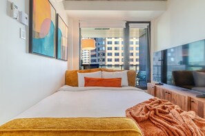 A hotel room with a bed, a TV, a window with a city view, and a door leading to a balcony. - Montreal Grand Escape | Free Parking & Pool (Montréal)