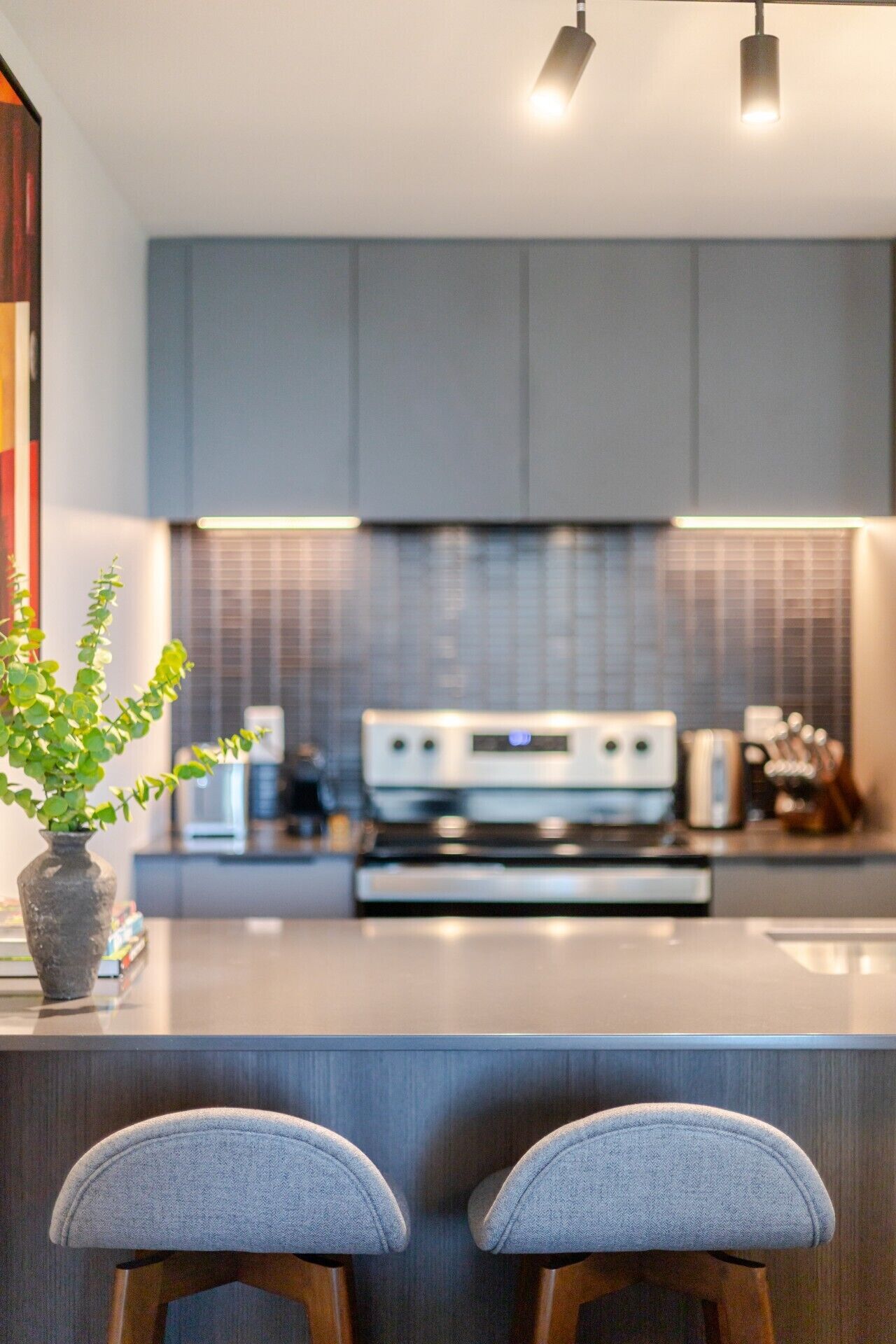 Eine moderne Küche mit einer zentralen Kochinsel, Barhocker und einem Blumentopf.
