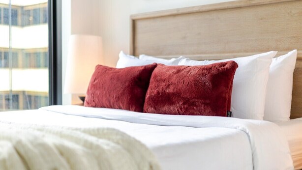 A hotel room with a bed, a headboard, and a window with a view of buildings. - Golden Stay | Free Parking & Pool (Montreal)