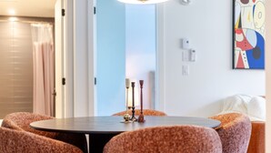 A dining area with a round table, four upholstered chairs, a modern pendant light, and a colorful abstract painting on the wall. - Golden Stay | Free Parking & Pool (Montreal)