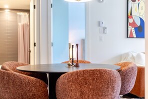 A dining area with a round table, four upholstered chairs, a modern pendant light, and a colorful abstract painting on the wall. - Golden Stay | Free Parking & Pool (Montreal)