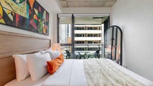 A hotel room with a bed, pillows, a blanket, a painting, a window, and a view of buildings. - Golden Stay | Free Parking & Pool (Montreal)