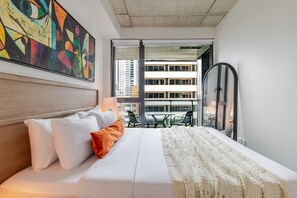 A hotel room with a bed, pillows, a blanket, a painting, a window, and a view of buildings. - Golden Stay | Free Parking & Pool (Montreal)
