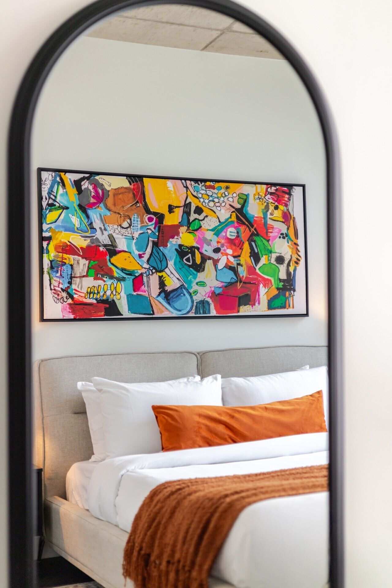 A bedroom with a bed, pillows, a headboard, and a colorful abstract painting above the bed.