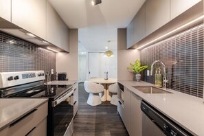 A modern kitchen with a built-in oven, a dishwasher, and a sink. There is a dining area with a round table and chairs. - Montreal Skyline Escape | Free Parking & Pool (Montreal)