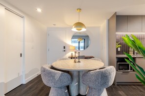 A modern dining area with a round table, grey upholstered chairs, a pendant light, and a view through a mirror. - Montreal Skyline Escape | Free Parking & Pool (Montreal)