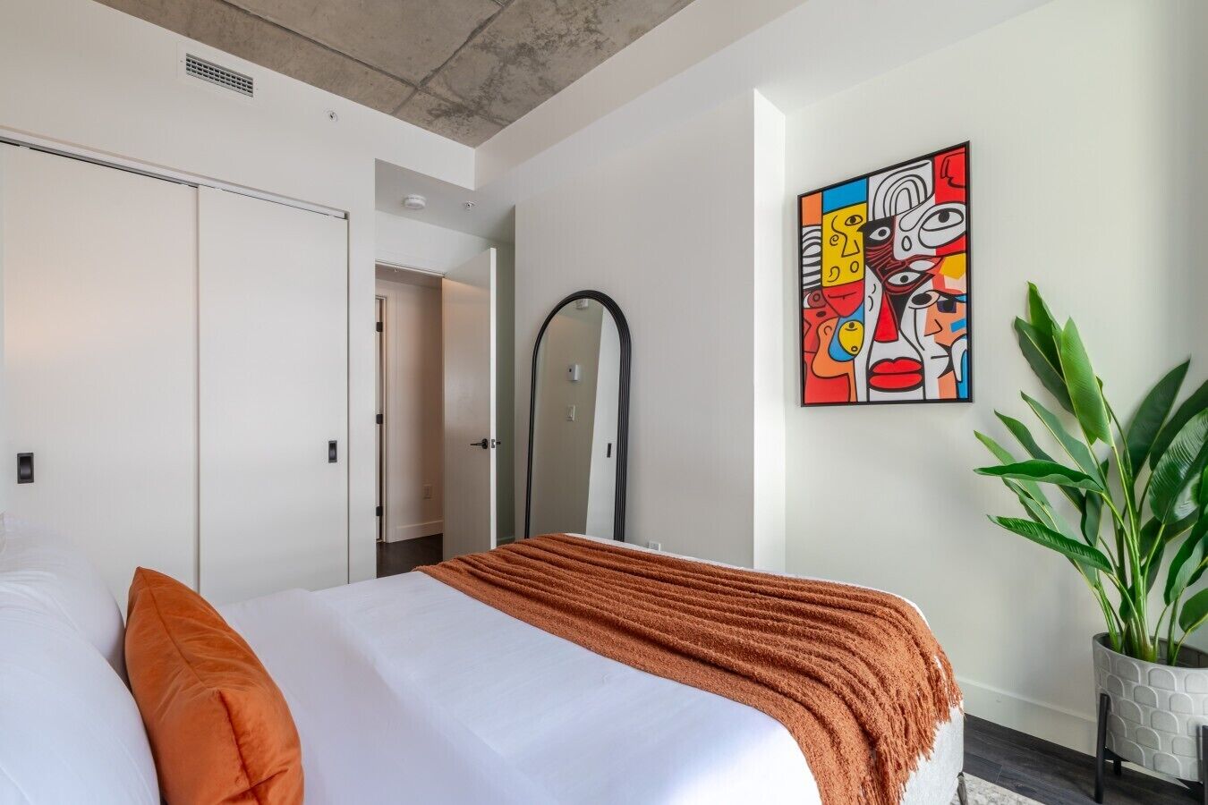 Habitación de hotel con cama, ducha, puerta, una obra de arte colgada en la pared y una planta en maceta.