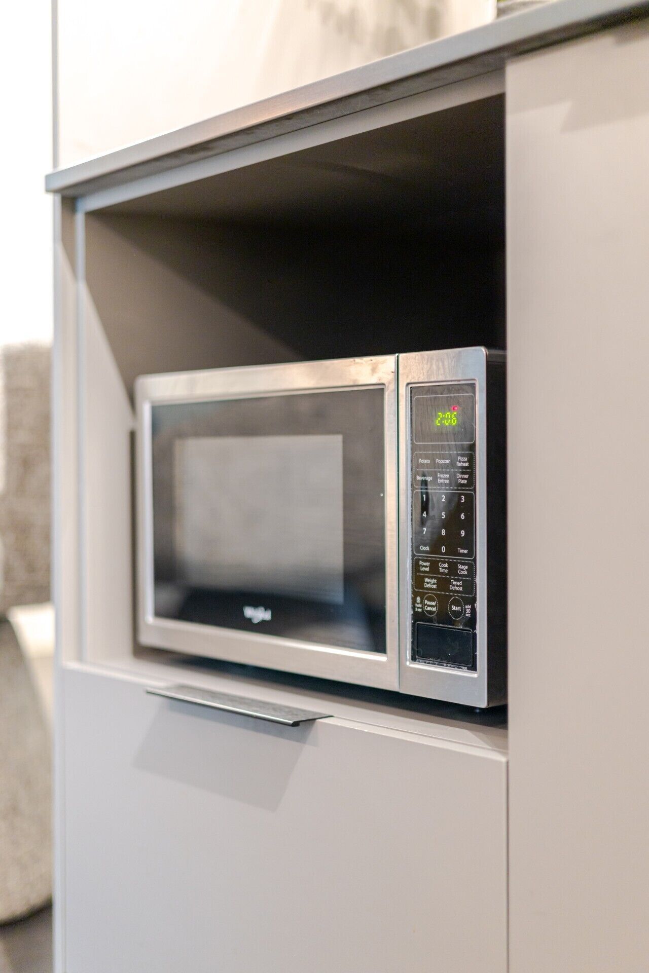 Eine Mikrowelle mit digitaler Anzeige und Bedienfeld, eingebaut in einem weißen Schrank.