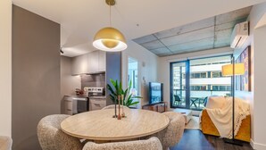 Ein modernes Wohnzimmer mit einem runden Esstisch, bequemen Sitzgelegenheiten, einem Fernseher und einem Balkon mit Blick.