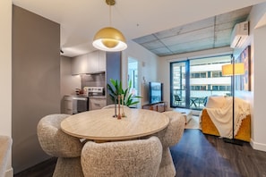 A modern living room with a round dining table, comfortable seating, a TV, and a balcony with a view. - Montreal Skyline Escape | Free Parking & Pool (Montreal)