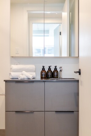A bathroom with a grey vanity, a mirror, and toiletries including hand soap, body soap, and shampoo. - Montreal Skyline Escape | Free Parking & Pool (Montreal)