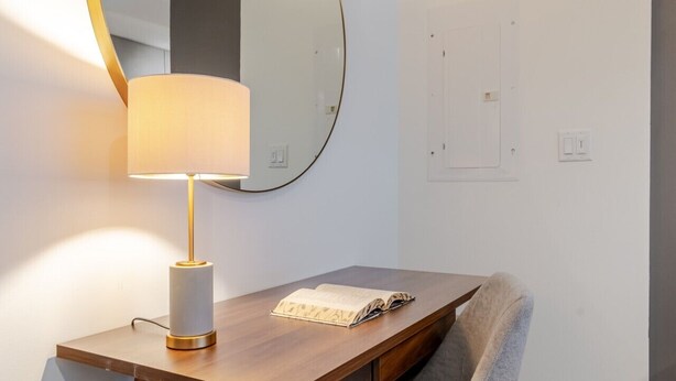 Ein modernes Zimmer mit Schreibtisch, Stuhl, Lampe und einem großen Spiegel.