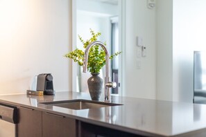 A modern kitchen with a stainless steel sink, a vase with green plants, and a coffee machine. - Downtown Poolside Haven | Free Parking & Pool (Montreal)