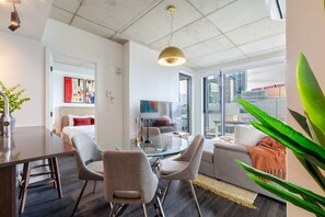A modern living room with a glass dining table, grey sofas, and a large window offering a city view. - Downtown Poolside Haven | Free Parking & Pool (Montreal)