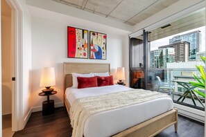 A modern hotel room with a large bed, two bedside lamps, abstract wall art, and a city view through a large window. - Downtown Poolside Haven | Free Parking & Pool (Montreal)