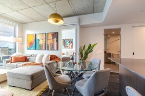Un salon moderne avec une table à manger en verre, des canapés gris et des œuvres d’art abstraites accrochées aux murs.