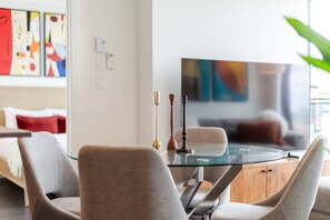 A modern living room with a glass dining table, two chairs, a flat-screen TV, and abstract art on the wall. - Downtown Poolside Haven | Free Parking & Pool (Montreal)