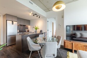 Une cuisine moderne avec un îlot central, un coin repas doté d’une table en verre et un salon avec un téléviseur.