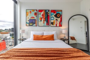 A hotel room with a large bed, two side tables, a mirror, and abstract artwork on the wall. - Downtown Poolside Haven | Free Parking & Pool (Montreal)