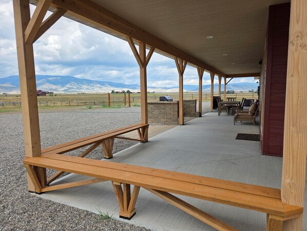 An outdoor covered patio with wooden beams, a concrete floor, and a view of a mountainous landscape. - Bear Claw Mountain House (Livingston)