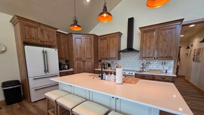 Een keuken met houten kastjes, een centraal eiland met krukken, hangende verlichting en een roestvrijstalen afzuigkap.