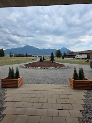 A paved area with a central gravel circle, surrounded by a gravel path and bordered by wooden planters with small trees. - Bear Claw Mountain House (Livingston)