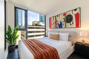 Ein Hotelzimmer mit einem großen Bett, Blick auf Gebäude und abstrakter Kunst an der Wand.