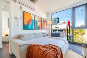 A modern hotel room with a large bed, city view, abstract art, and a window with a view of buildings. - Luxury Urban Retreat | Pools Gym Sauna & Balcony (Montreal)