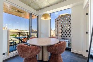 A modern room with a round table, two chairs, a pendant light, large windows, and a view of the cityscape. - Luxury Urban Retreat | Pools Gym Sauna & Balcony (Montreal)
