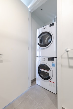 A laundry room with two stacked front-loading washing machines. - Luxury Urban Retreat | Pools Gym Sauna & Balcony (Montreal)