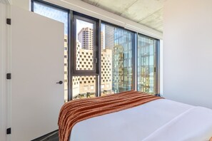 Un dormitorio con un ventanal grande, una cama y vistas a edificios.
