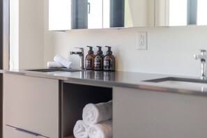 A bathroom with a sink, three bottles of shampoo, and towels. - Luxury Urban Retreat | Pools Gym Sauna & Balcony (Montreal)