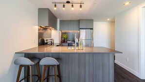 Une cuisine moderne dotée d’un îlot central, de tabourets de bar, d’appareils électroménagers en acier inoxydable et d’un luminaire au design contemporain.