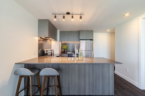 A modern kitchen with a central island, bar stools, stainless steel appliances, and a contemporary light fixture. - Luxury Urban Retreat | Pools Gym Sauna & Balcony (Montreal)