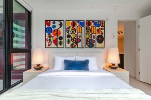 Ein Hotelzimmer mit einem großen Bett, zwei Nachttischen, einem Fenster und drei abstrakten Bildern an der Wand.