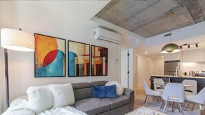 Uma sala de estar moderna com um sofá, uma mesa de jantar com cadeiras e arte abstrata na parede.